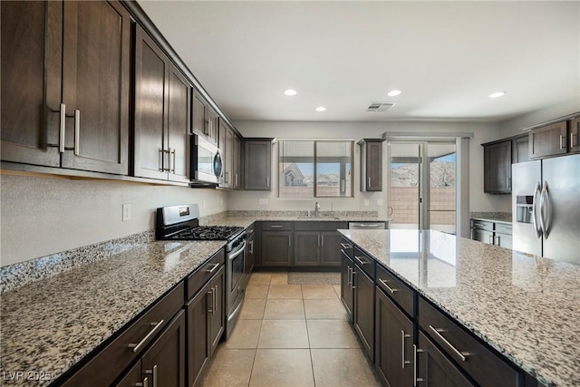 kitchen featuring visible vents, appliances with stainless steel finishes, a sink, dark brown cabinetry, and light stone countertops