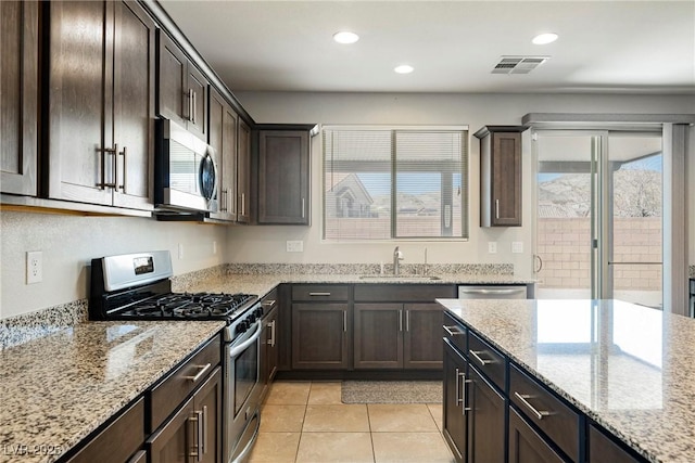 kitchen featuring light stone counters, stainless steel appliances, visible vents, a sink, and dark brown cabinets