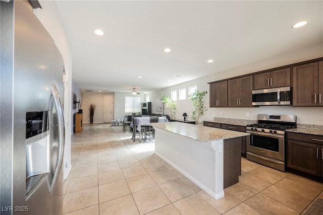 kitchen with dark brown cabinetry, light stone countertops, stainless steel appliances, and open floor plan