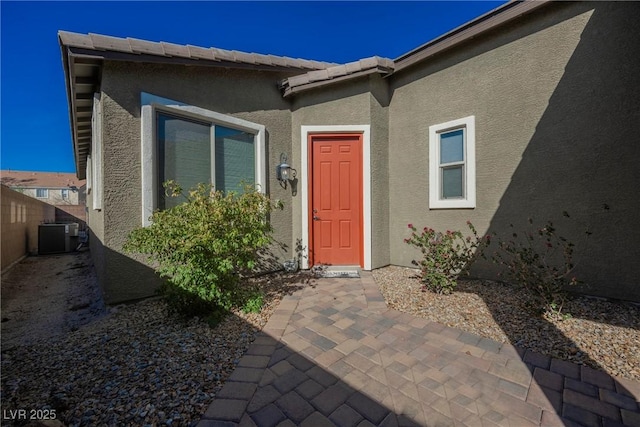 doorway to property featuring a tile roof, a patio, stucco siding, central AC, and fence