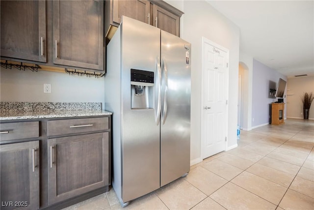 kitchen with light stone counters, light tile patterned floors, open floor plan, dark brown cabinetry, and stainless steel fridge with ice dispenser