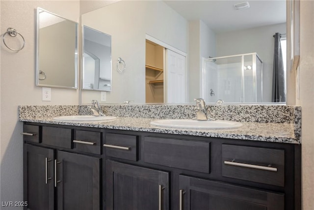 full bathroom featuring double vanity, a shower stall, a walk in closet, and a sink