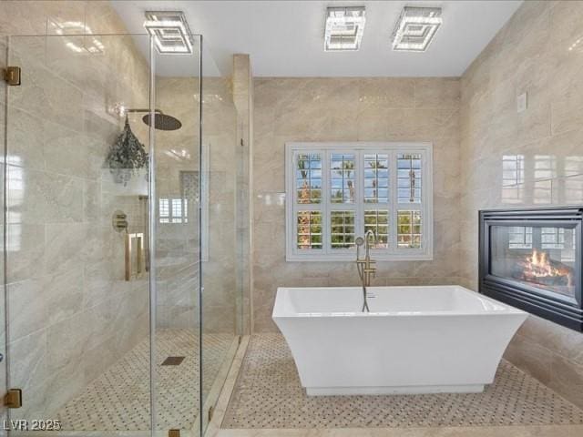 full bathroom with a glass covered fireplace, a freestanding tub, tile walls, and a shower stall