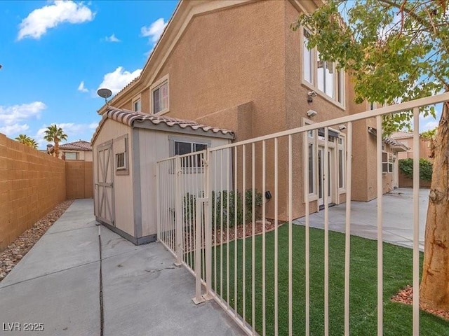 view of gate featuring an outbuilding, a patio, a lawn, and fence private yard