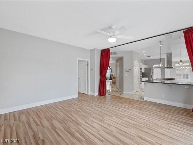 unfurnished living room with light wood-style flooring, visible vents, a ceiling fan, baseboards, and stairway