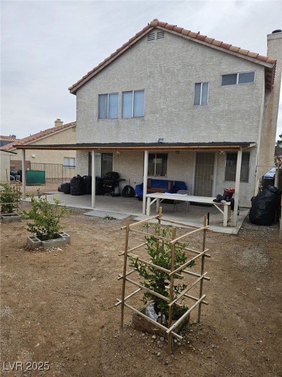 rear view of house with a patio area, a tile roof, a chimney, and stucco siding