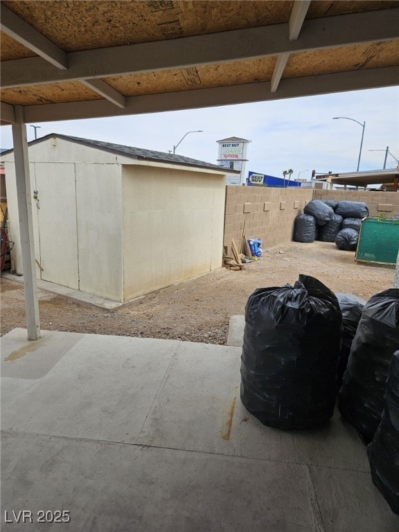 view of patio with fence, a storage unit, and an outbuilding