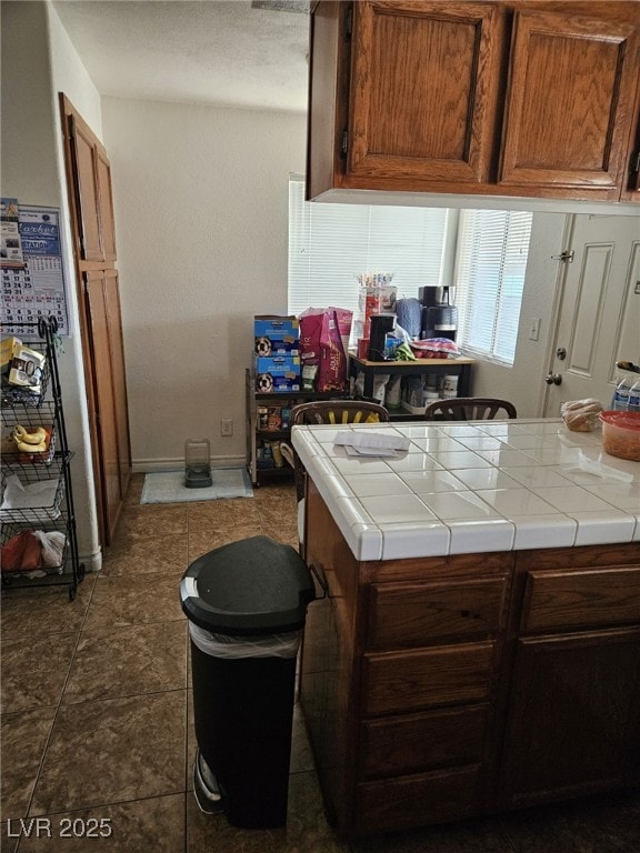 kitchen with tile countertops, dark tile patterned floors, brown cabinetry, and baseboards