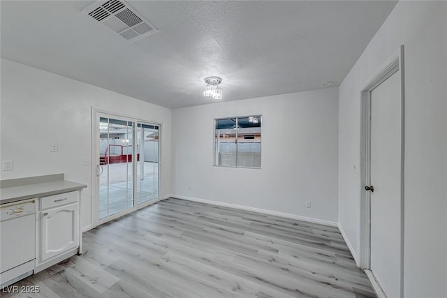 unfurnished dining area with baseboards, a textured ceiling, visible vents, and light wood-style floors