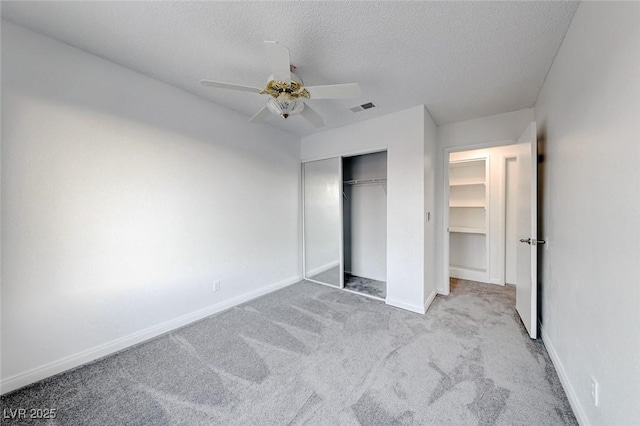 unfurnished bedroom featuring baseboards, visible vents, light colored carpet, a textured ceiling, and a closet