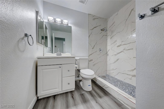 bathroom with a textured wall, toilet, wood finished floors, vanity, and a shower stall