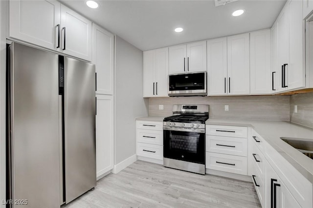 kitchen with stainless steel appliances, light wood-style floors, white cabinets, light countertops, and decorative backsplash