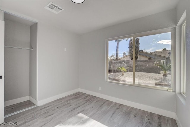 unfurnished bedroom with a closet, wood finished floors, visible vents, and baseboards