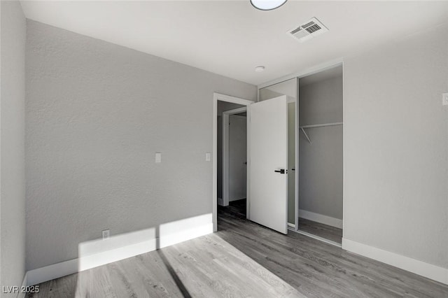 unfurnished bedroom with a closet, wood finished floors, visible vents, and baseboards