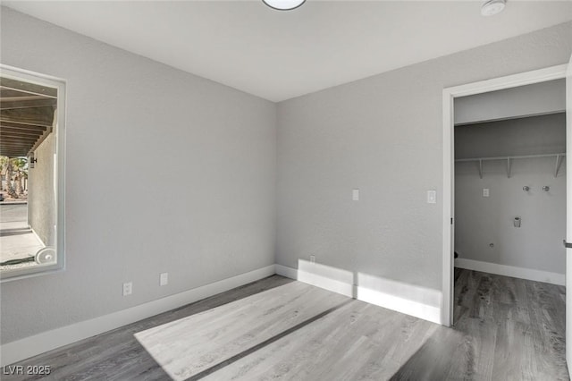 unfurnished bedroom featuring dark wood-style floors, baseboards, and a walk in closet