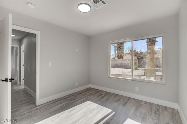 empty room featuring light wood finished floors, baseboards, and visible vents