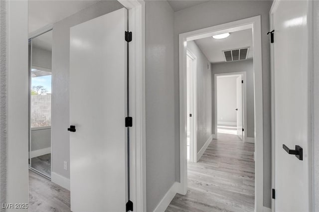 corridor featuring baseboards, visible vents, and light wood finished floors