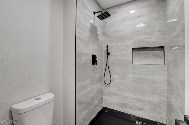 full bathroom with toilet, tiled shower, and a textured wall