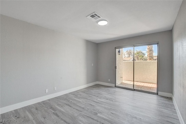 spare room featuring light wood-type flooring, visible vents, and baseboards