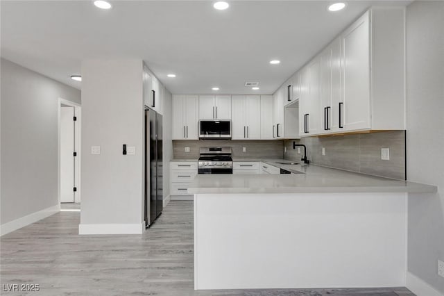 kitchen featuring white cabinets, a peninsula, stainless steel appliances, light countertops, and a sink