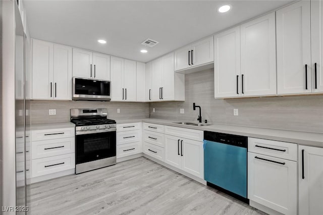 kitchen with light countertops, appliances with stainless steel finishes, a sink, and white cabinets