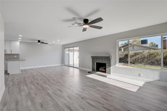 unfurnished living room with a brick fireplace, light wood-style flooring, baseboards, and ceiling fan