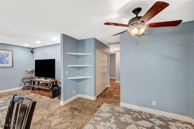 living room featuring stone finish floor, ceiling fan, and baseboards