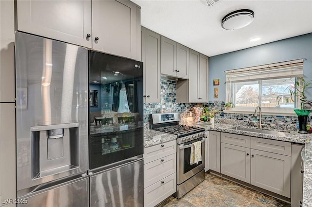 kitchen with appliances with stainless steel finishes, a sink, light stone counters, and gray cabinetry