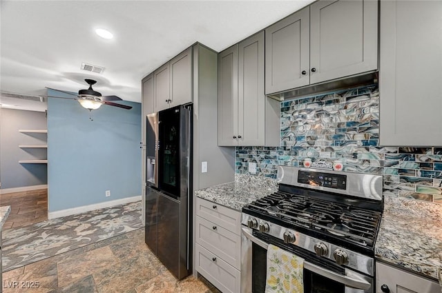 kitchen featuring light stone counters, under cabinet range hood, stainless steel appliances, baseboards, and decorative backsplash