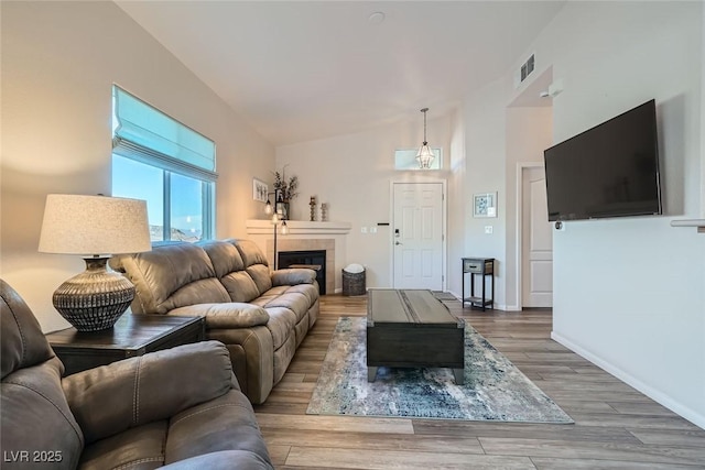 living room featuring a fireplace, visible vents, wood finished floors, high vaulted ceiling, and baseboards