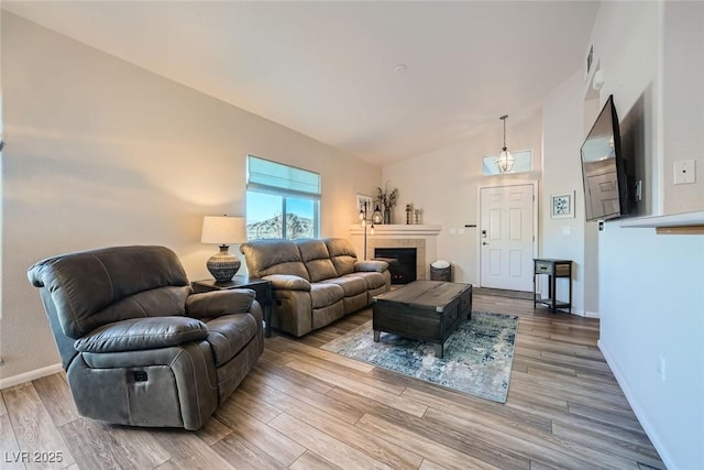 living room featuring a tiled fireplace, baseboards, and wood finished floors