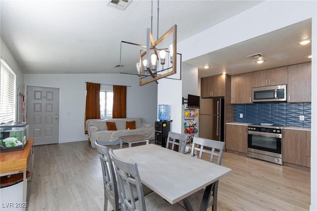 dining space featuring vaulted ceiling, light wood-style flooring, a textured ceiling, and visible vents