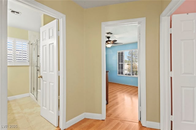 hall with light wood-style floors, visible vents, and baseboards