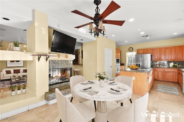 kitchen with backsplash, light tile patterned flooring, a kitchen island, stainless steel fridge, and a multi sided fireplace