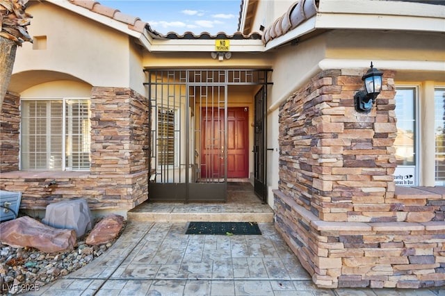 doorway to property featuring stone siding, a tile roof, and stucco siding