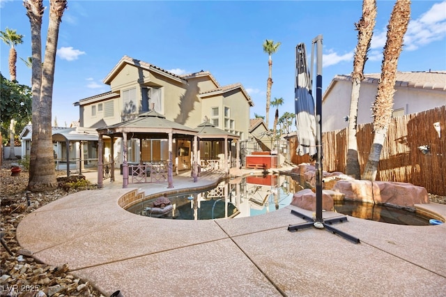 back of house with an outdoor pool, a patio, fence, a gazebo, and stucco siding