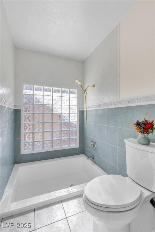 bathroom with toilet, tile patterned flooring, tile walls, and tiled shower