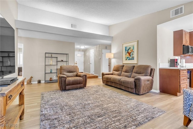 living room featuring light wood-type flooring, visible vents, and a textured ceiling