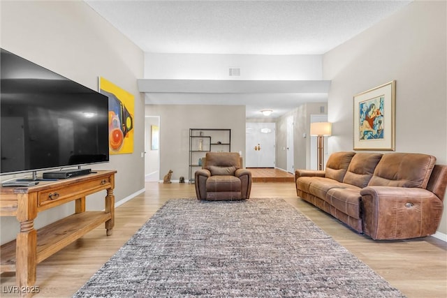 living area featuring visible vents, baseboards, a textured ceiling, and light wood finished floors