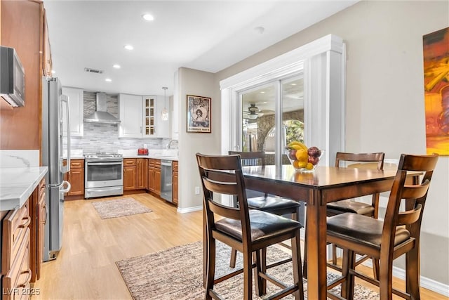 kitchen with brown cabinets, decorative backsplash, appliances with stainless steel finishes, light wood-style floors, and wall chimney range hood