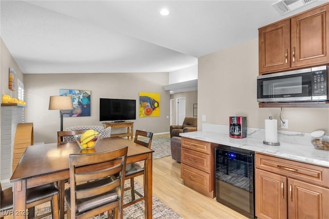 kitchen with beverage cooler, stainless steel microwave, brown cabinets, open floor plan, and light stone counters