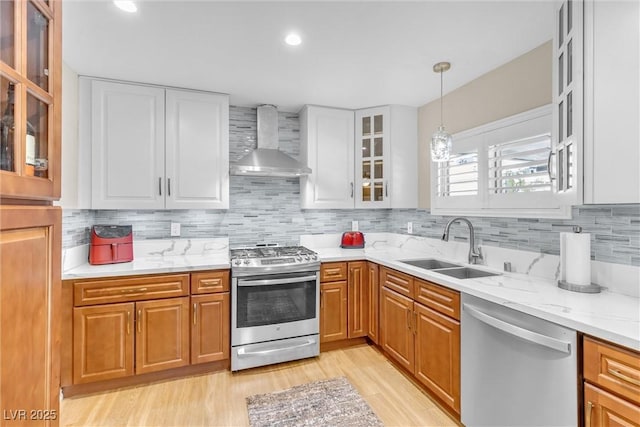 kitchen with appliances with stainless steel finishes, glass insert cabinets, white cabinetry, a sink, and wall chimney exhaust hood