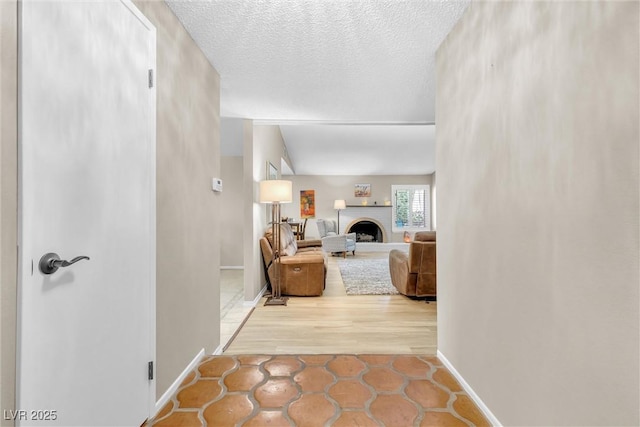 living area with a fireplace with raised hearth, a textured ceiling, and baseboards