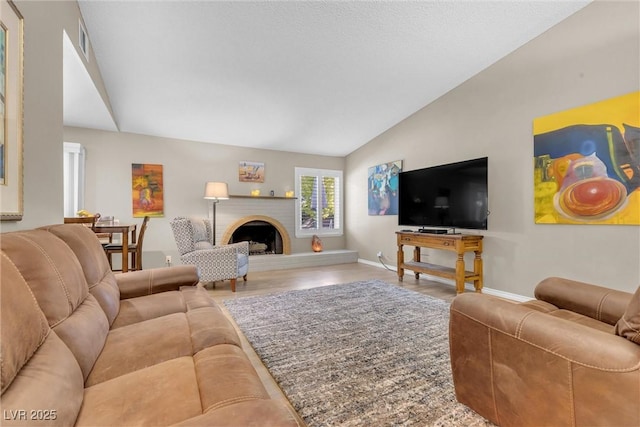 living area featuring lofted ceiling, wood finished floors, visible vents, baseboards, and a brick fireplace