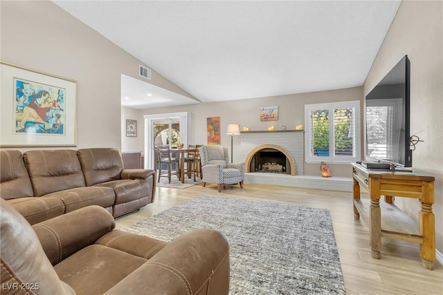 living room with lofted ceiling, a brick fireplace, visible vents, and light wood-style flooring