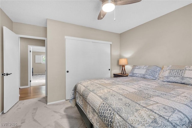 bedroom with a ceiling fan, a closet, light colored carpet, and baseboards