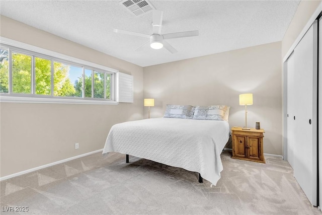 bedroom with visible vents, light colored carpet, ceiling fan, a textured ceiling, and a closet