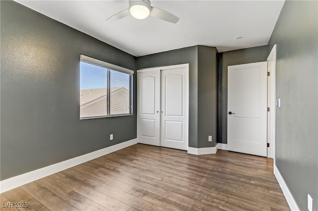 unfurnished bedroom with a closet, wood finished floors, a ceiling fan, and baseboards