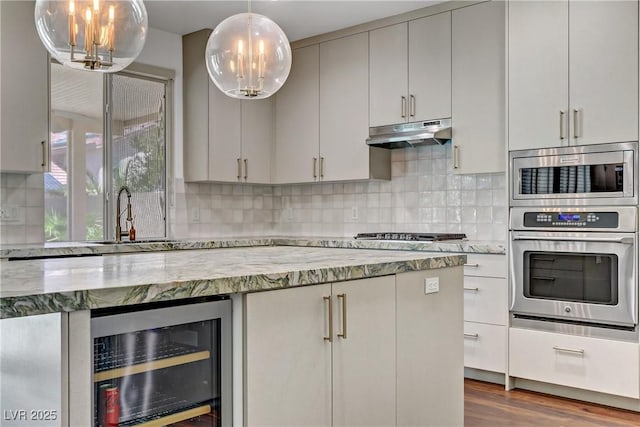 kitchen featuring light stone counters, under cabinet range hood, beverage cooler, appliances with stainless steel finishes, and decorative light fixtures