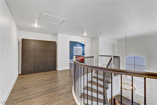 hallway featuring attic access, baseboards, wood finished floors, and an upstairs landing